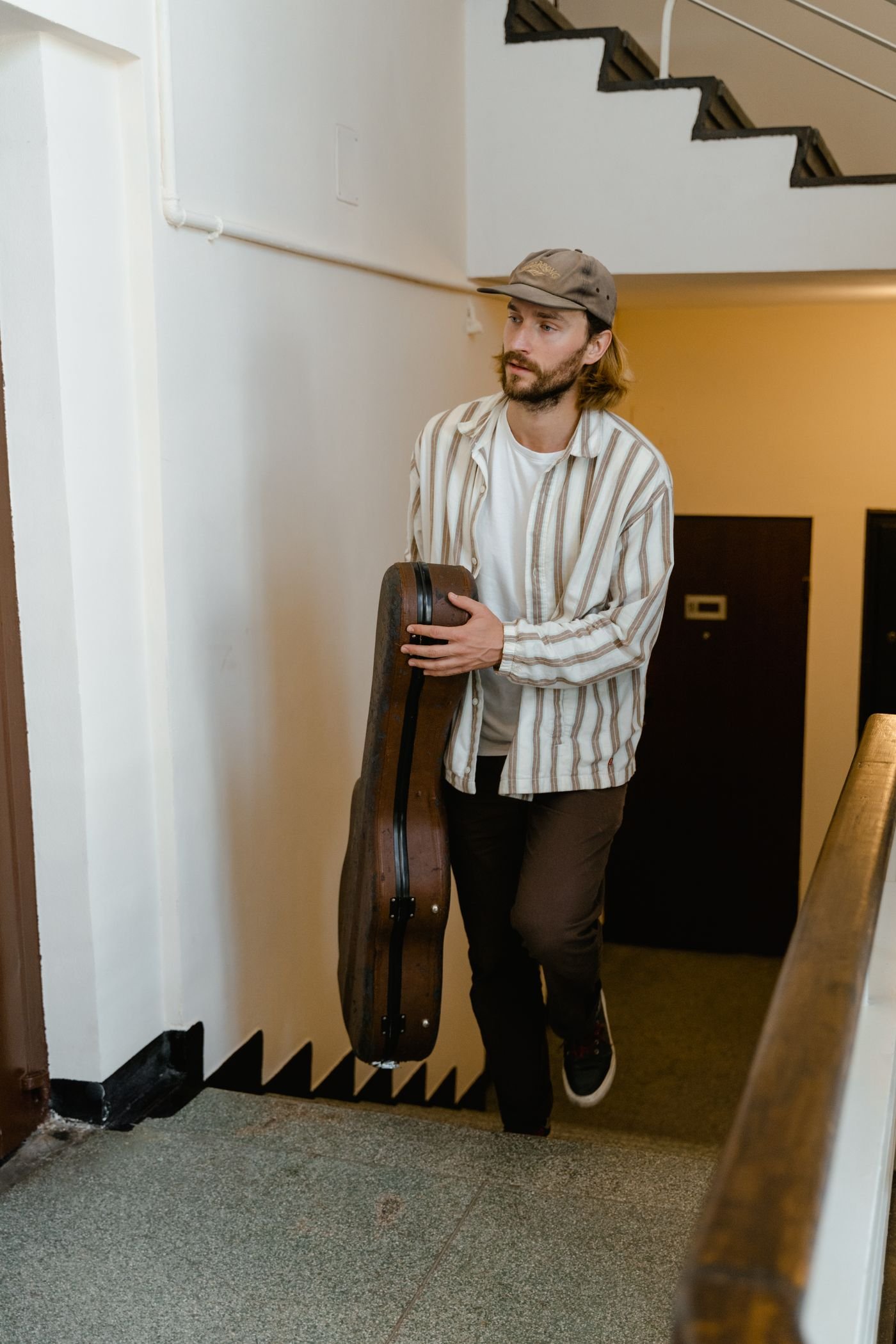 Man carrying a guitar case up an indoor stairwell