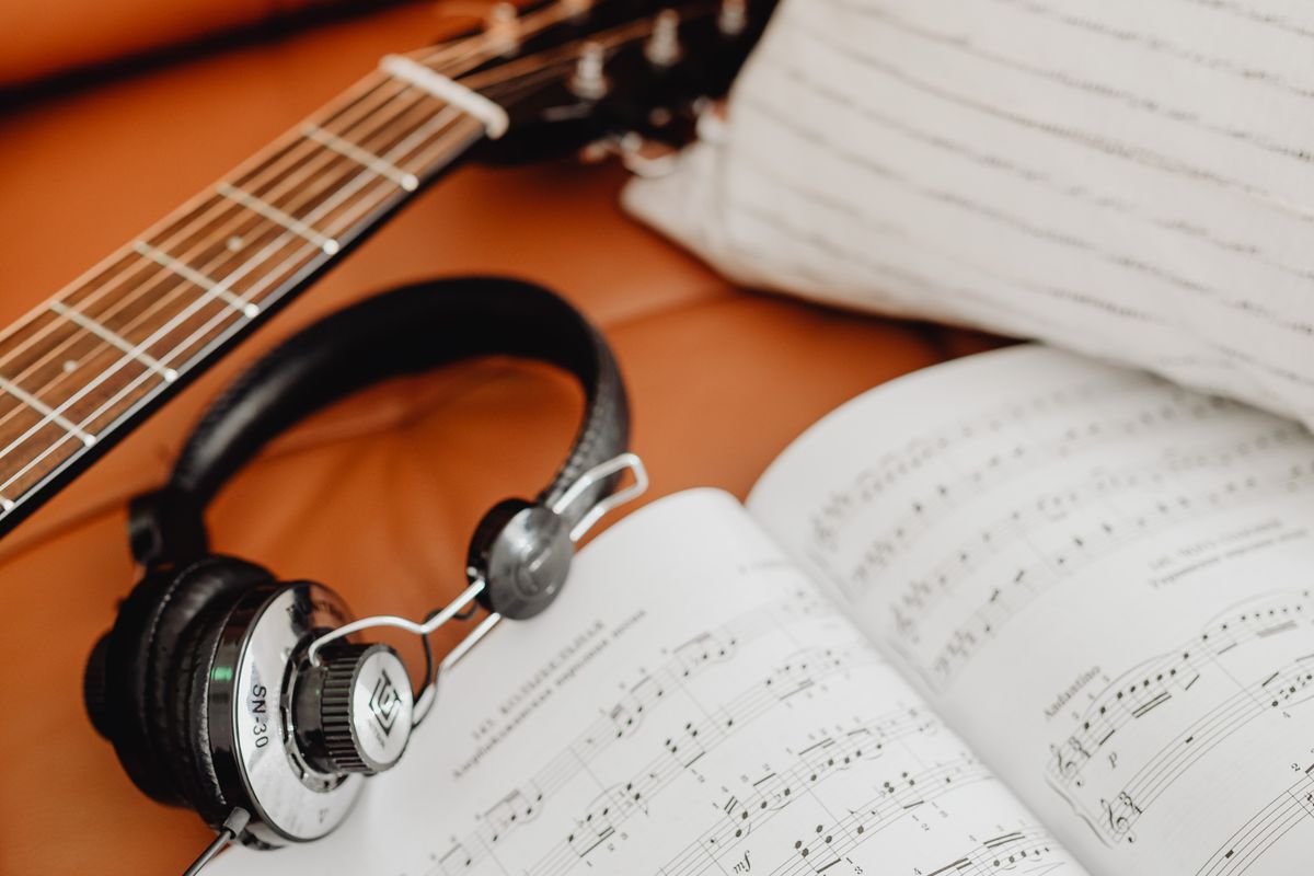 Headphones resting against a guitar neck next to open sheet music