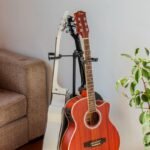 Two acoustic-electric travel guitars on wall-mounted stands in a real living room