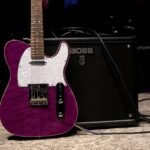A purple electric guitar leaning against a BOSS combo amplifier on stage