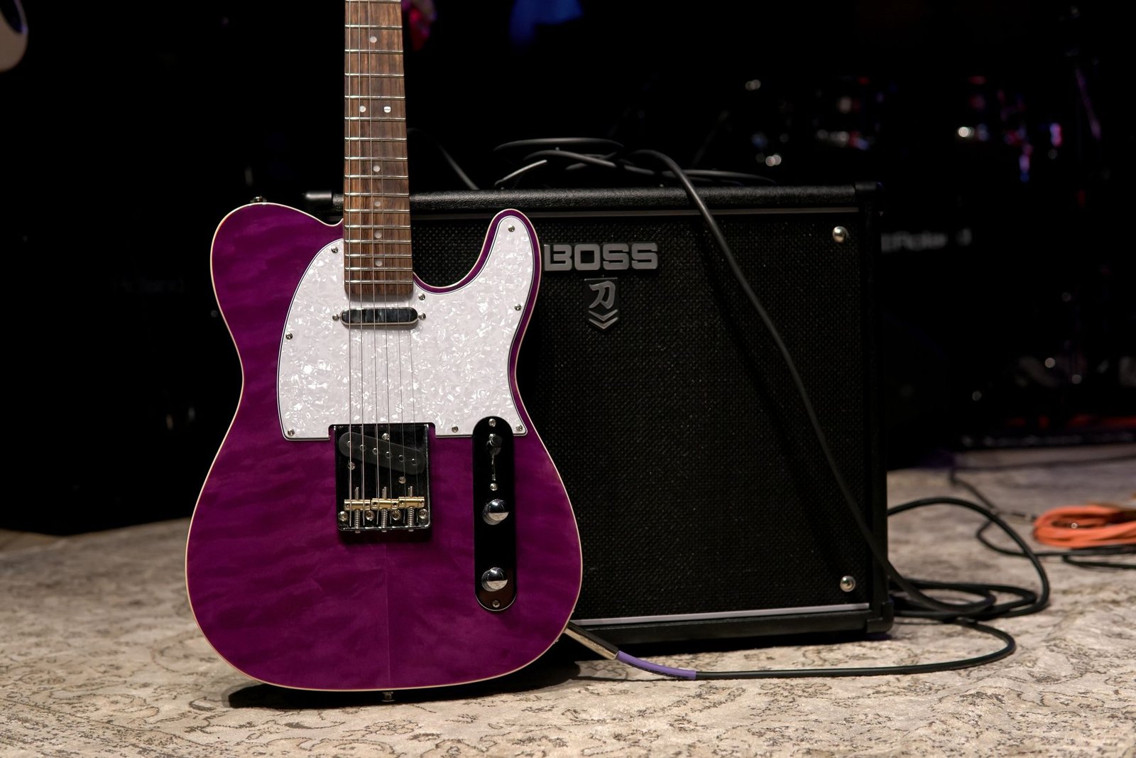 A purple electric guitar leaning against a BOSS combo amplifier on stage
