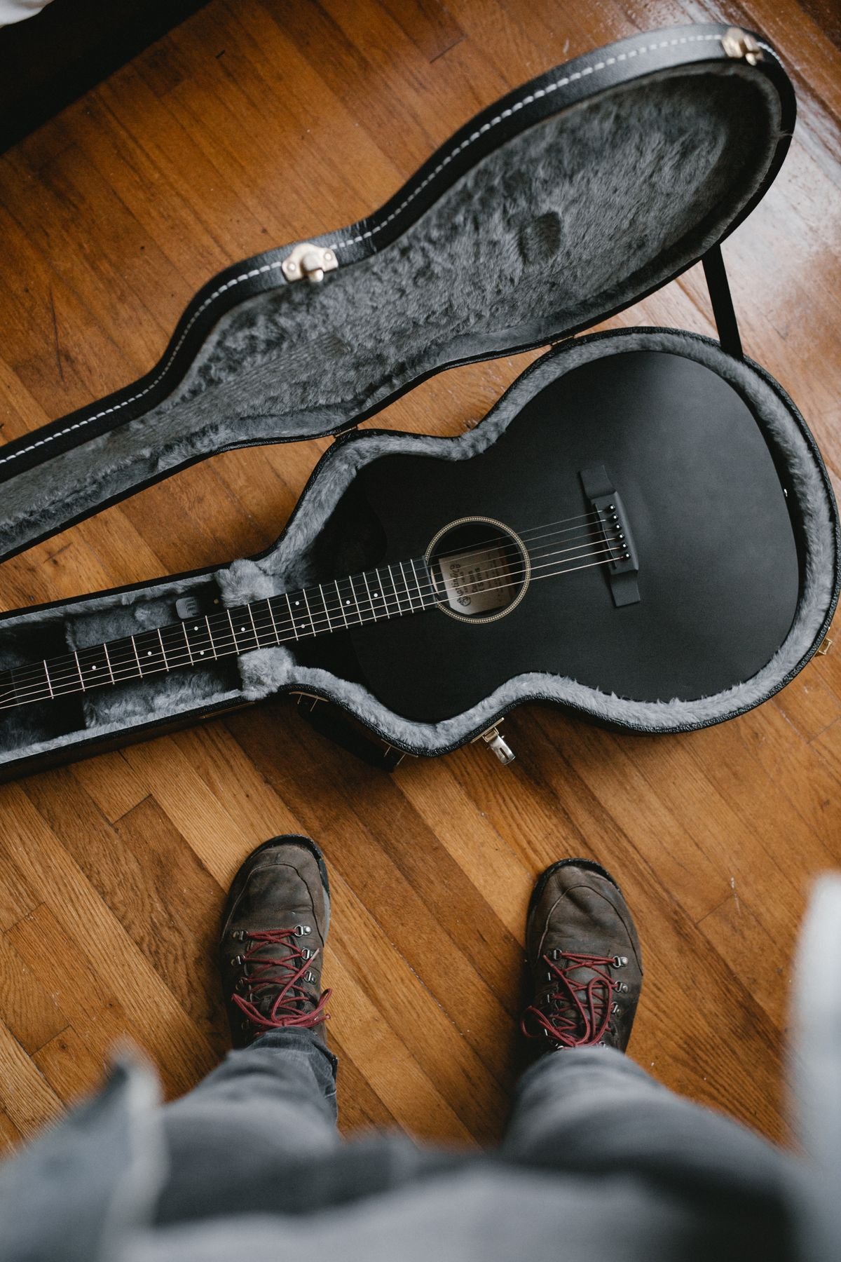 Small-bodied acoustic guitar resting in an open hard case with plush grey lining, illustrating a travel guitar case