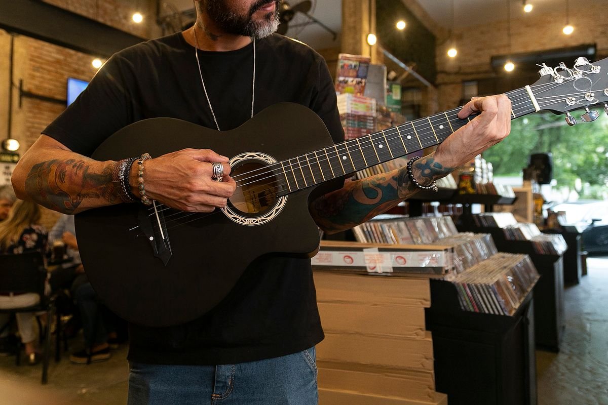 Person playing a small dark-bodied acoustic guitar in a record shop, illustrating the compact scale of a half-size travel guitar