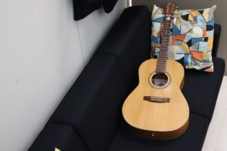 Compact-bodied acoustic guitar resting on a sofa, illustrating the half-size dreadnought shape of a mini travel acoustic