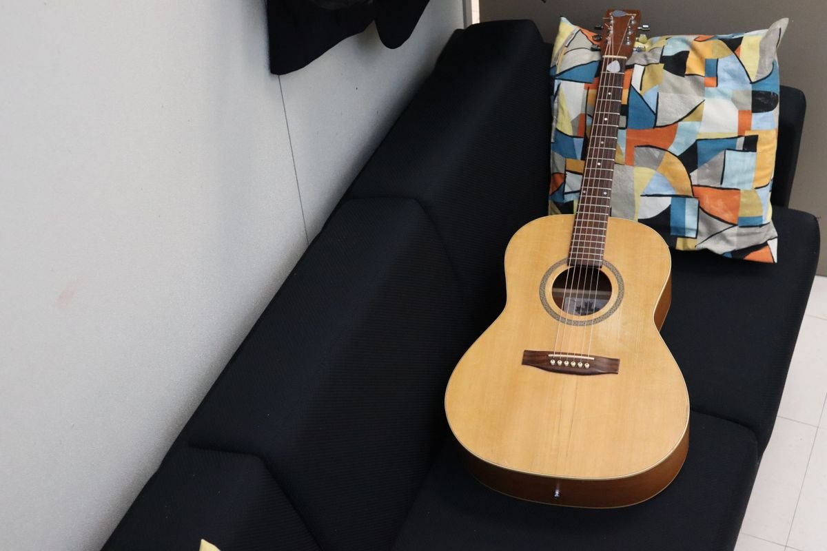 Compact-bodied acoustic guitar resting on a sofa, illustrating the half-size dreadnought shape of a mini travel acoustic