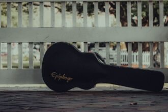 A guitar case resting against a white fence on a pavement, waiting to travel
