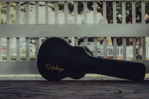 A guitar case resting against a white fence on a pavement, waiting to travel