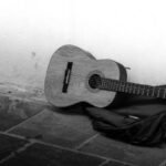 Acoustic guitar and gig bag lying on a worn floor against a bare wall