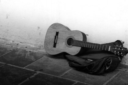 Acoustic guitar and gig bag lying on a worn floor against a bare wall
