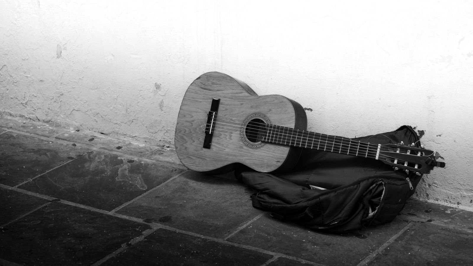 Acoustic guitar and gig bag lying on a worn floor against a bare wall