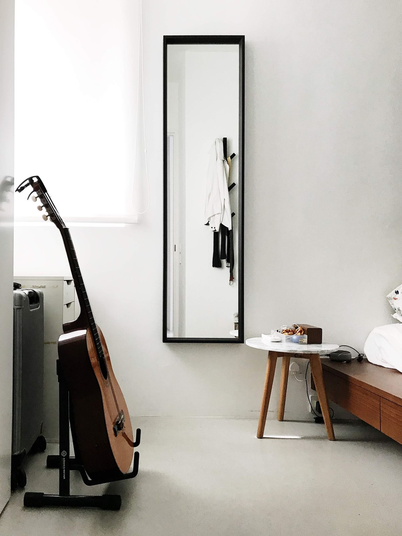 Acoustic guitar on a stand next to a suitcase in a sparsely furnished room
