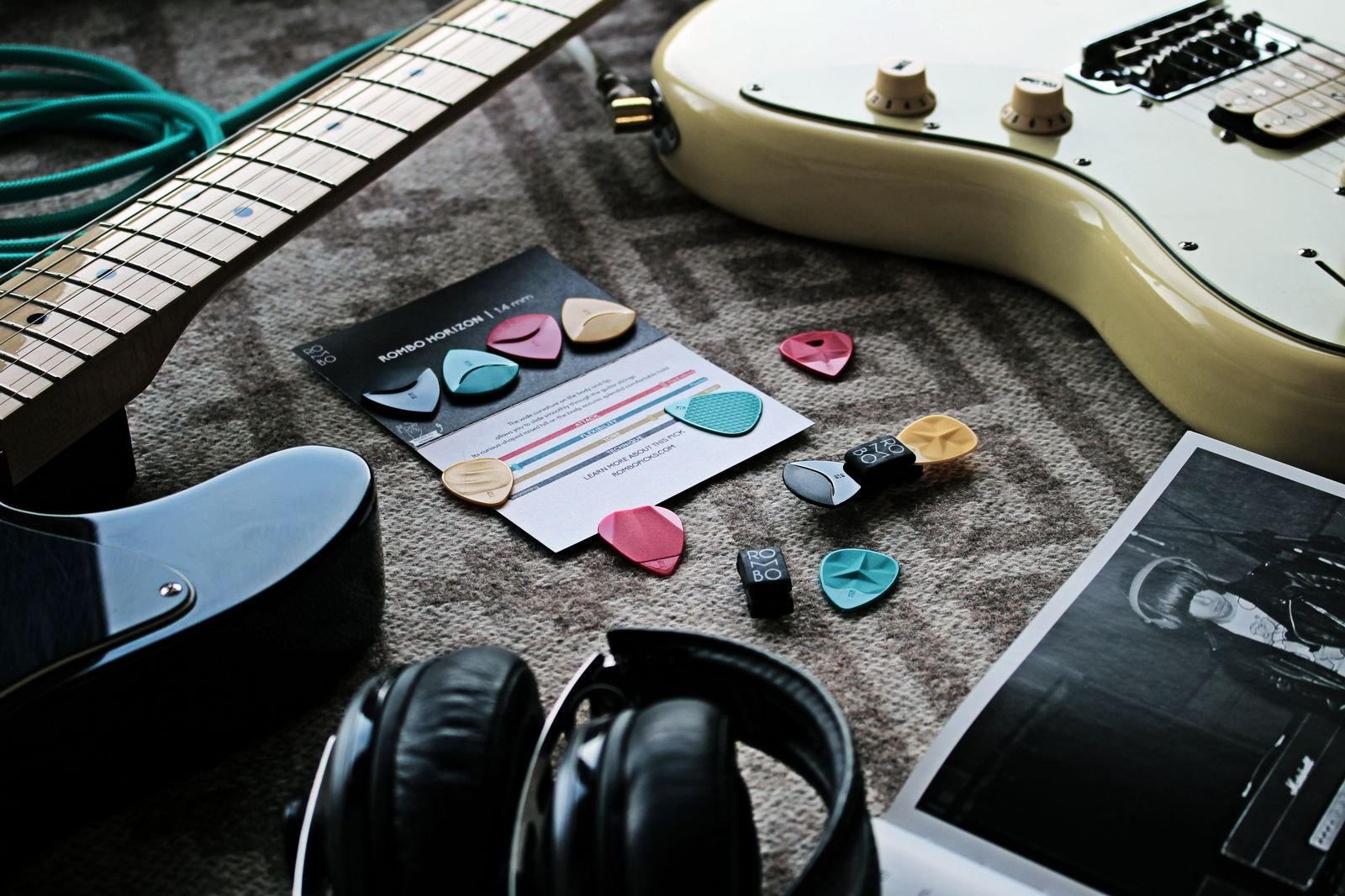 Assortment of guitar picks and small accessories laid out beside an electric guitar