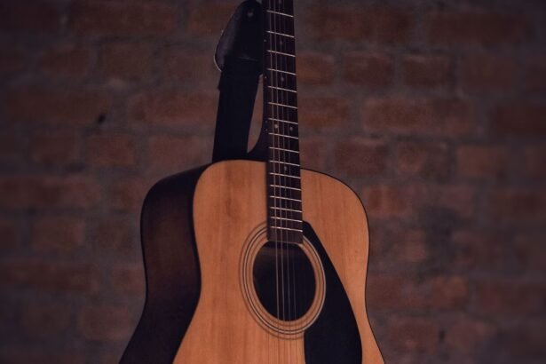 Natural-finish steel-string acoustic guitar hanging by its strap against a brick wall, showing the full body and neck