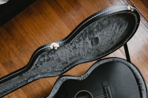 A matte black acoustic guitar resting in an open hardshell case with plush grey lining, illustrating a travel guitar kit