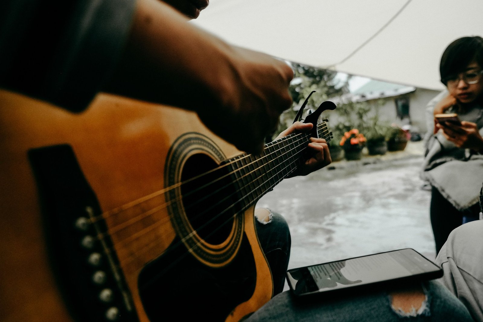 Close-up of hands playing an acoustic guitar next to a tablet screen, illustrating app-connected guitar practice