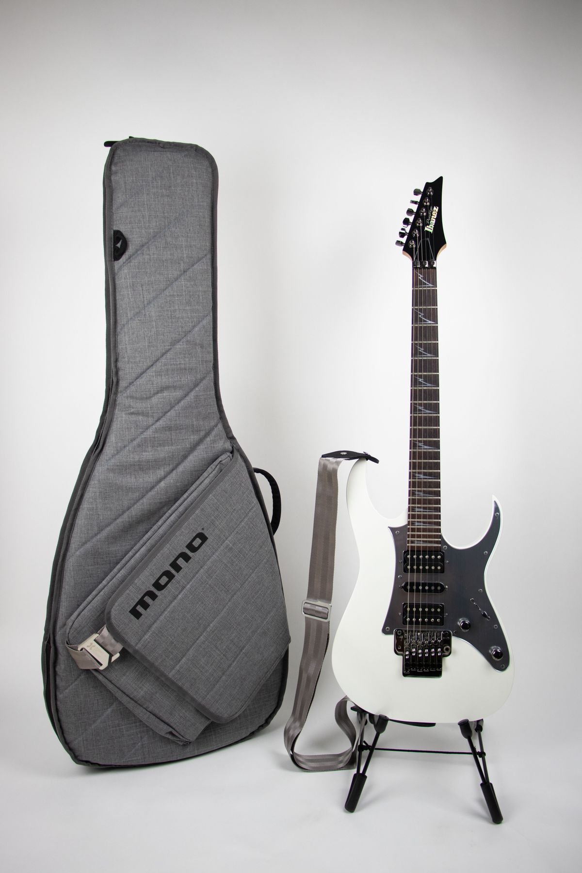 Padded grey gig bag for an electric guitar standing next to a guitar stand