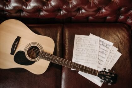 Small-bodied acoustic guitar with sheet music on a leather sofa, illustrating a compact travel-friendly acoustic