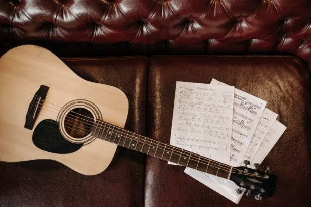 Small-bodied acoustic guitar with sheet music on a leather sofa, illustrating a compact travel-friendly acoustic