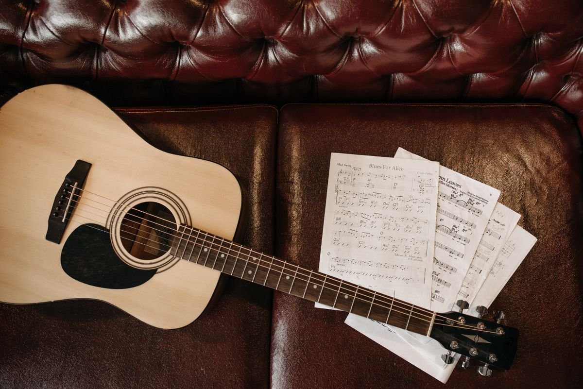 Small-bodied acoustic guitar with sheet music on a leather sofa, illustrating a compact travel-friendly acoustic
