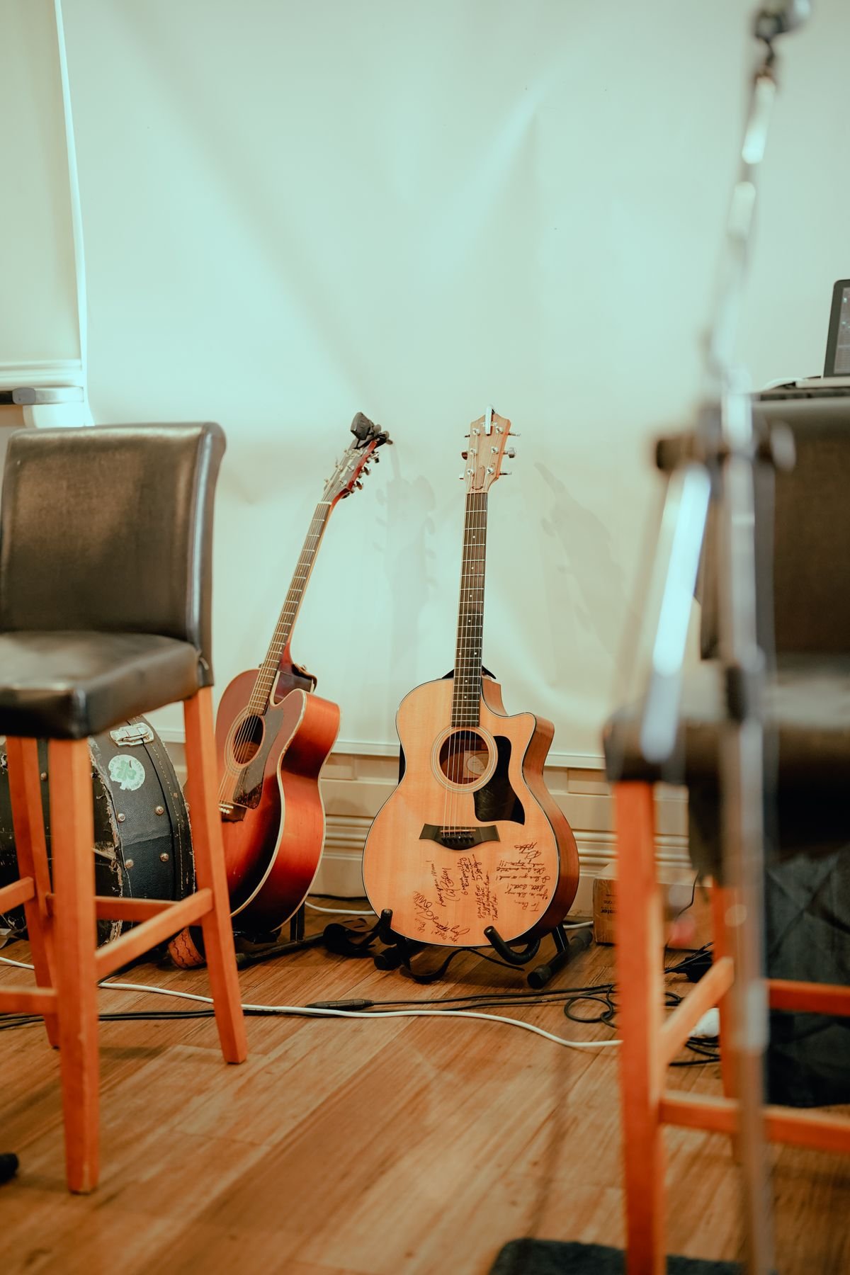 Two acoustic guitars leaning against a wall in a rehearsal room, the kind of everyday setting a small-bodied travel acoustic actually lives in