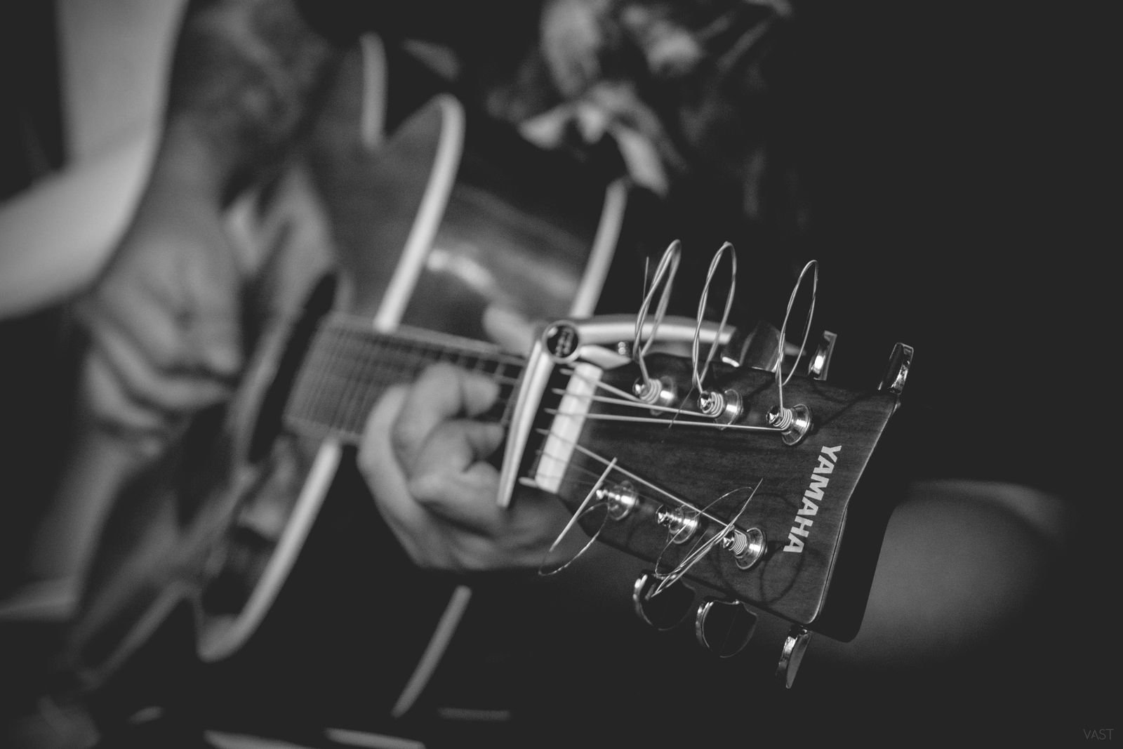 Black and white close-up of a hand fretting a chord on a Yamaha acoustic guitar