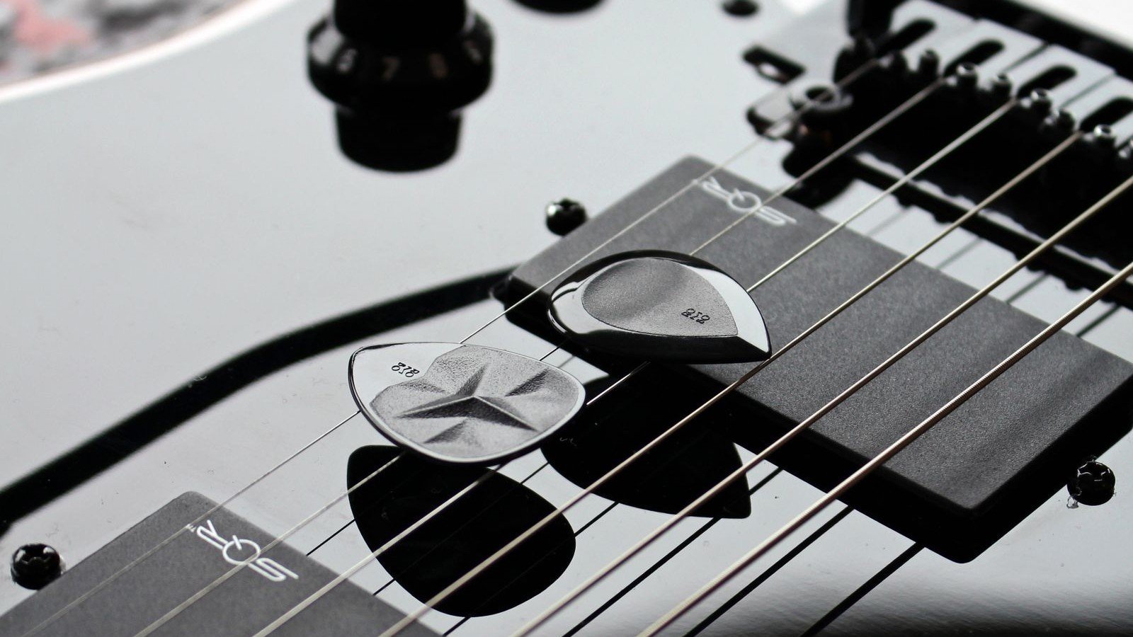 Two guitar picks resting on the pickups and strings of a black solid-body electric guitar with chrome hardware