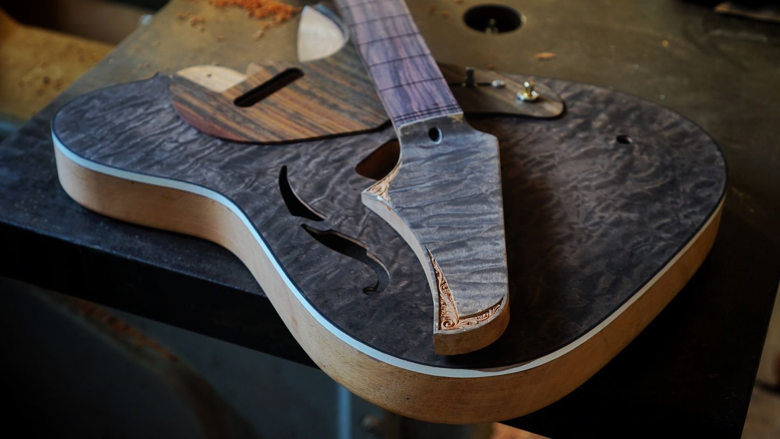 Close-up of a figured guitar body and neck joint on a workbench, showing the kind of premium tonewood construction the EART GW2 is built around