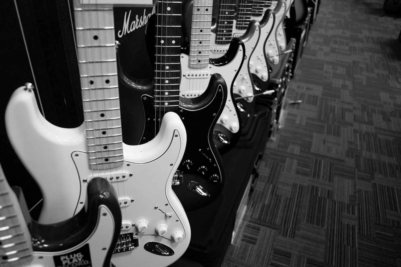 A row of Stratocaster-shaped electric guitars hanging on a music shop wall