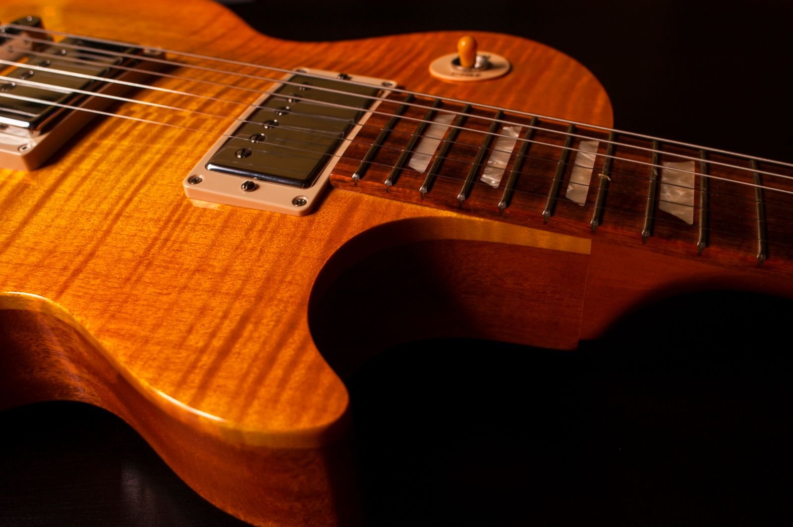 Close-up detail of an electric guitar humbucker pickup and bridge on a flame-top solid body