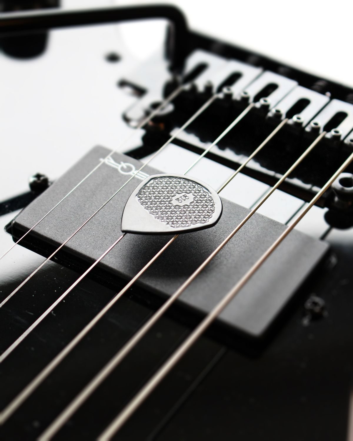 Close-up of an electric guitar's bridge and humbucker pickup with a guitar pick resting on the strings