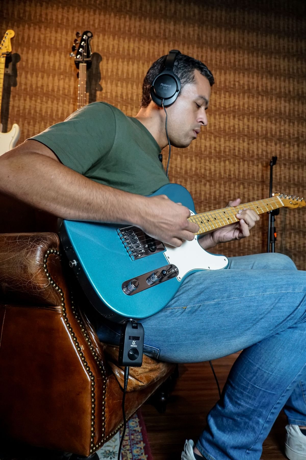 A guitarist practising on an electric guitar while wearing headphones, seated in a home studio