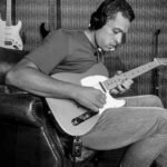 A guitarist playing an electric guitar through headphones in a home studio, illustrating silent practice with a built-in headphone amp
