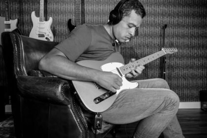 A guitarist playing an electric guitar through headphones in a home studio, illustrating silent practice with a built-in headphone amp