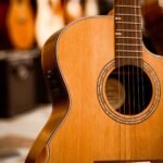 A cutaway acoustic guitar hanging in a guitar shop with other guitars blurred behind it
