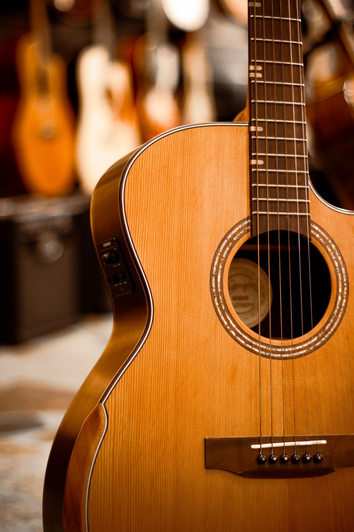 A cutaway acoustic guitar hanging in a guitar shop with other guitars blurred behind it
