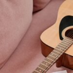 A mahogany acoustic-electric travel guitar body and neck resting on a sofa