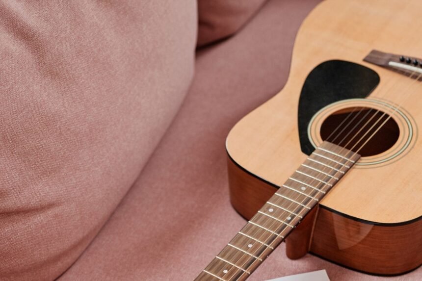 A mahogany acoustic-electric travel guitar body and neck resting on a sofa