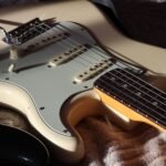 Close-up of a Stratocaster-shaped guitar body showing single-coil pickups and control knobs