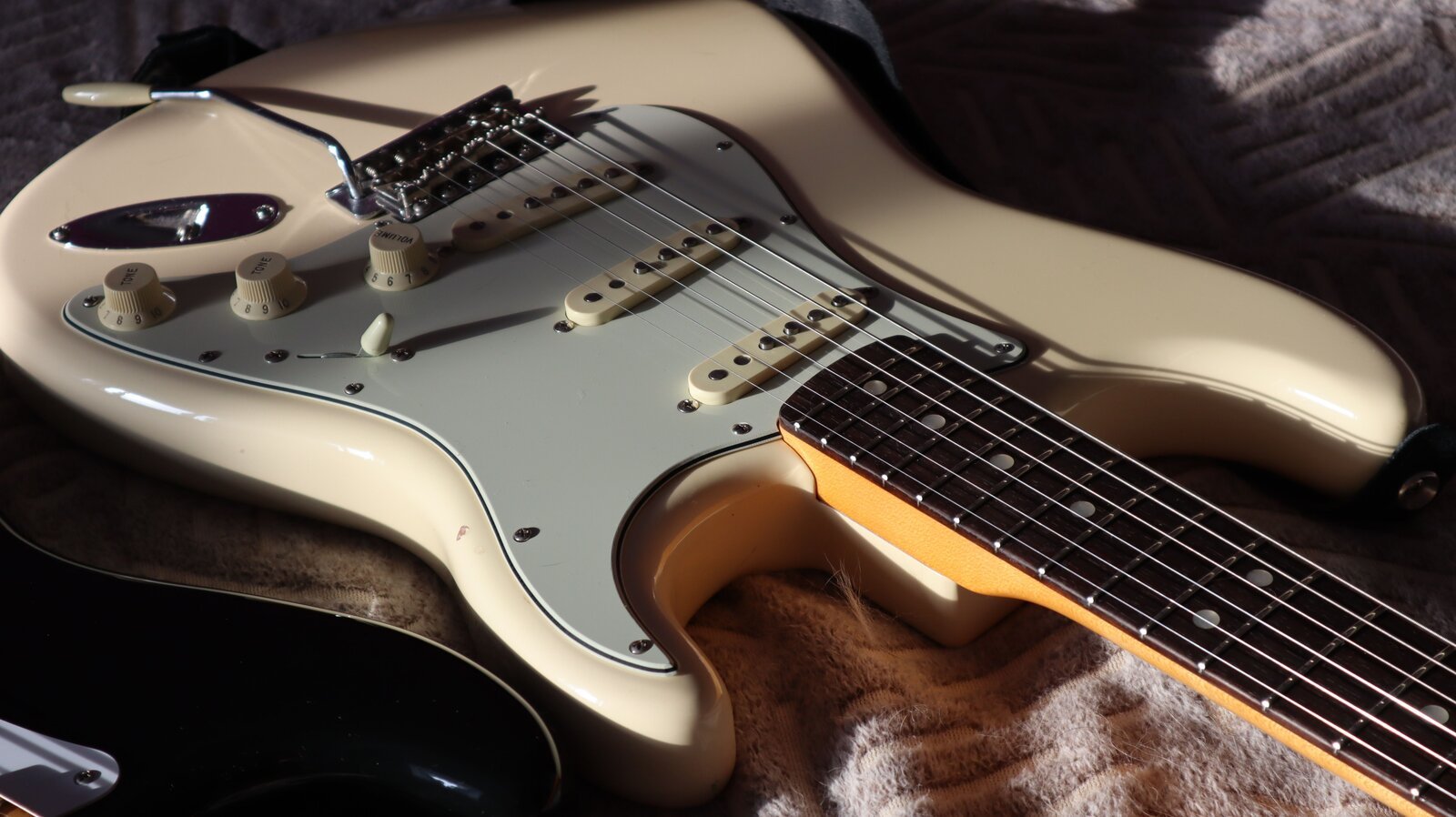 Close-up of a Stratocaster-shaped guitar body showing single-coil pickups and control knobs