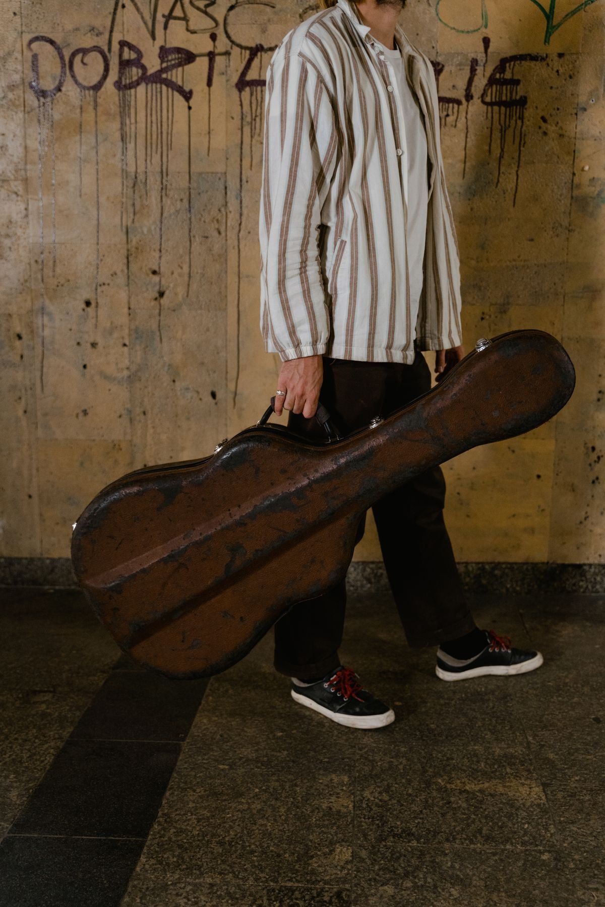 A person carrying a hard-shell guitar case down a city street