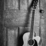 A small-bodied acoustic guitar leaning against a weathered wooden door, showing its compact parlour-style proportions
