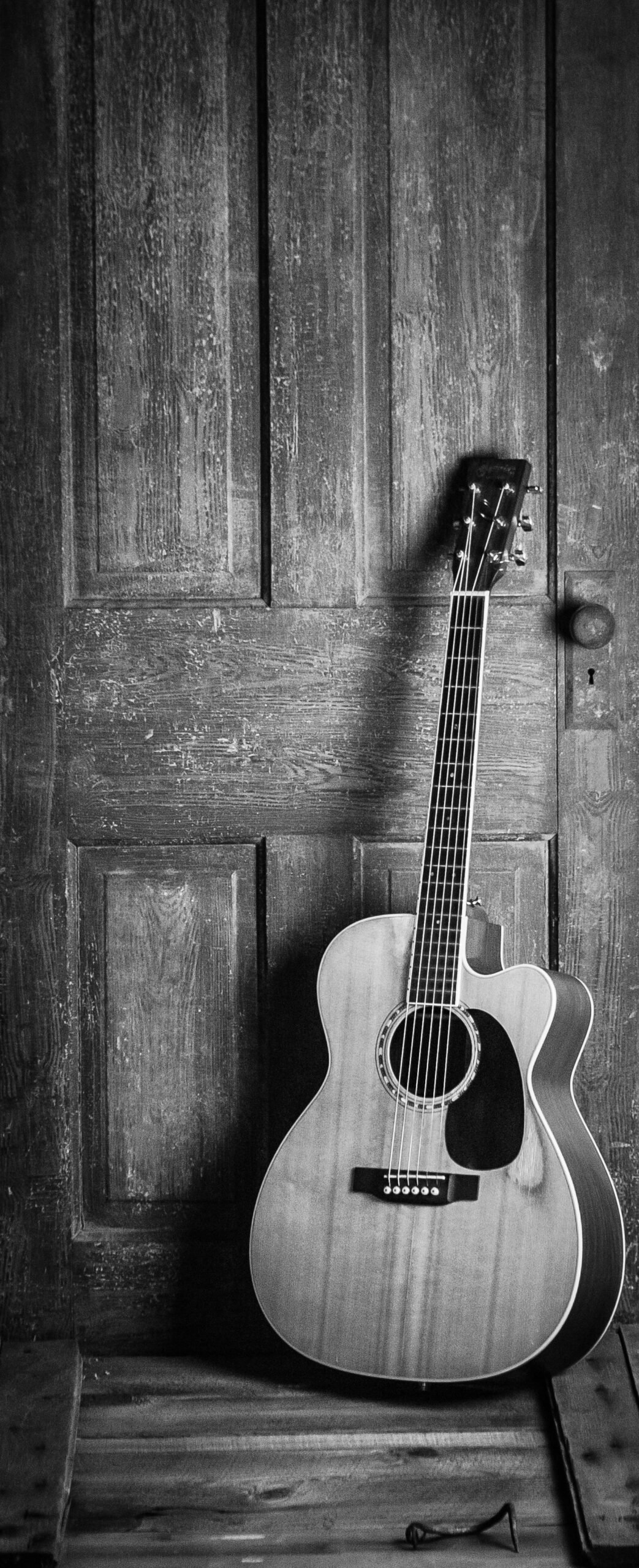 A small-bodied acoustic guitar leaning against a weathered wooden door, showing its compact parlour-style proportions