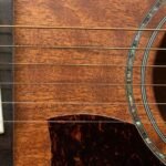 Close-up of a guitar bridge and abalone-ringed soundhole on a warm honey-toned wood body