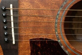 Close-up of a guitar bridge and abalone-ringed soundhole on a warm honey-toned wood body