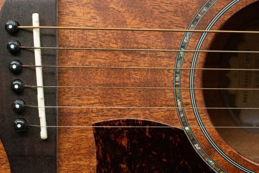Close-up of a guitar bridge and abalone-ringed soundhole on a warm honey-toned wood body