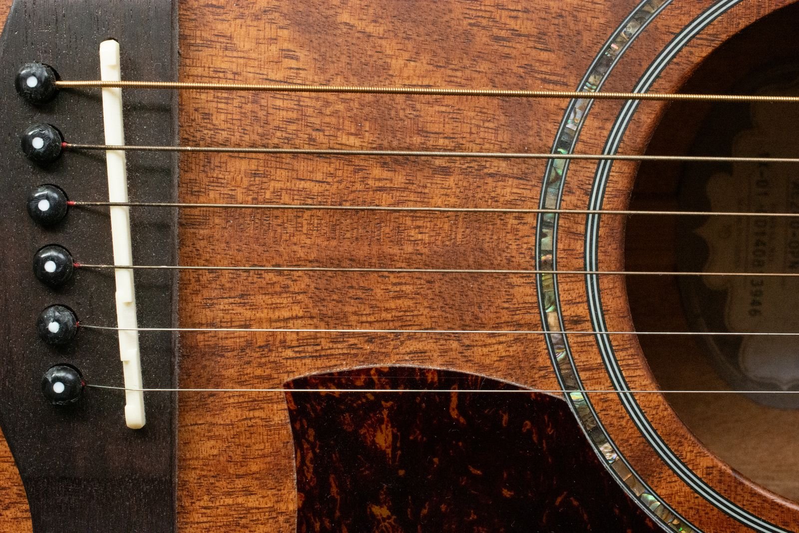 Close-up of a guitar bridge and abalone-ringed soundhole on a warm honey-toned wood body