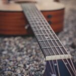 A small acoustic guitar body and neck resting on gravel outdoors