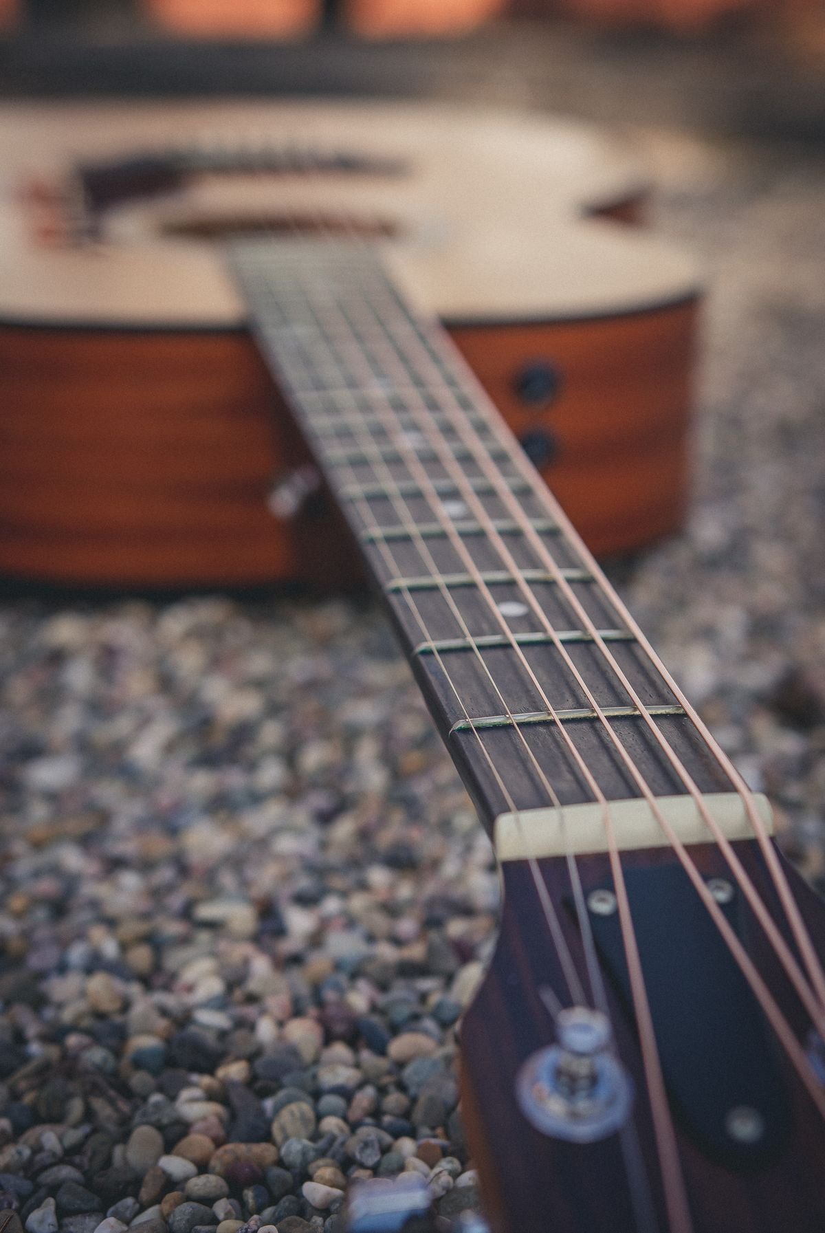 A small acoustic guitar body and neck resting on gravel outdoors