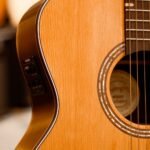 Solid spruce-top compact acoustic guitar with a side-mounted piezo pickup preamp, other guitars visible in a shop rack behind it