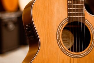 Solid spruce-top compact acoustic guitar with a side-mounted piezo pickup preamp, other guitars visible in a shop rack behind it